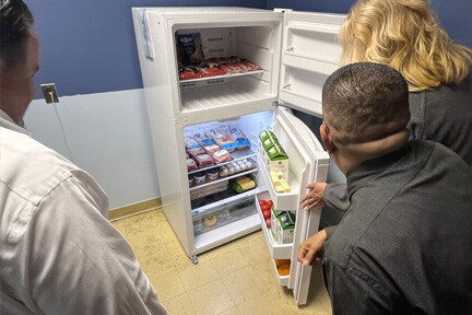 Three people opening a community fridge packed with food