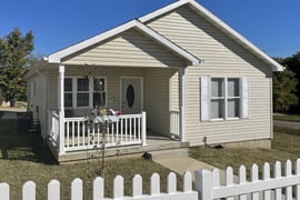 The front of a home with pale yellow siding and a picket fence