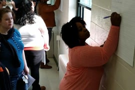 An adult writes on a piece of paper tacked to the wall