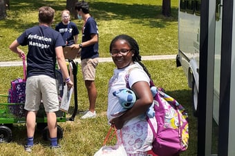 A child with a backpack smiles on her way off a bus