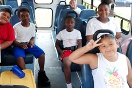 Elementary school aged children smile and pose on a bus to camp