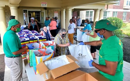 Residents in summer clothing and employees in green shirts and hats browse through bags